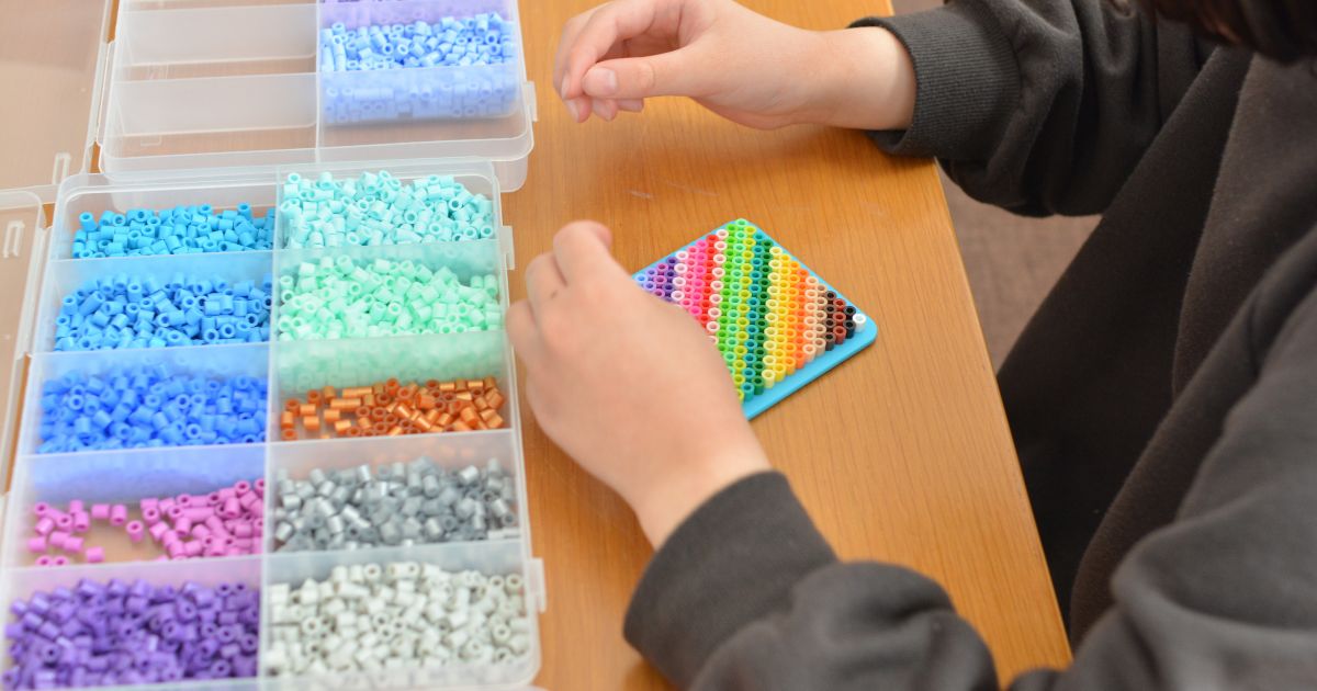 子どもがアイロンビーズケースから色を選びながら作品を作っている様子